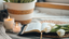 Two candles, a bible and some white tulips are on a table with a potted plant.