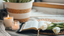 Two candles, a bible and some white tulips are on a table with a potted plant. 