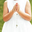 Little girl in a white dress, hands are in a prayer gesture and holding a white photo rosary.