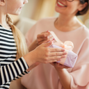 Mother and daughter looking at each other and smiling while daughter holds a lavender wrapped present. -desktop