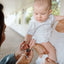 Mom holding baby while baby holds a blue and white baptism rosary gift. 