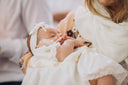 Mother holding baby in a white baptism gown. -desktop